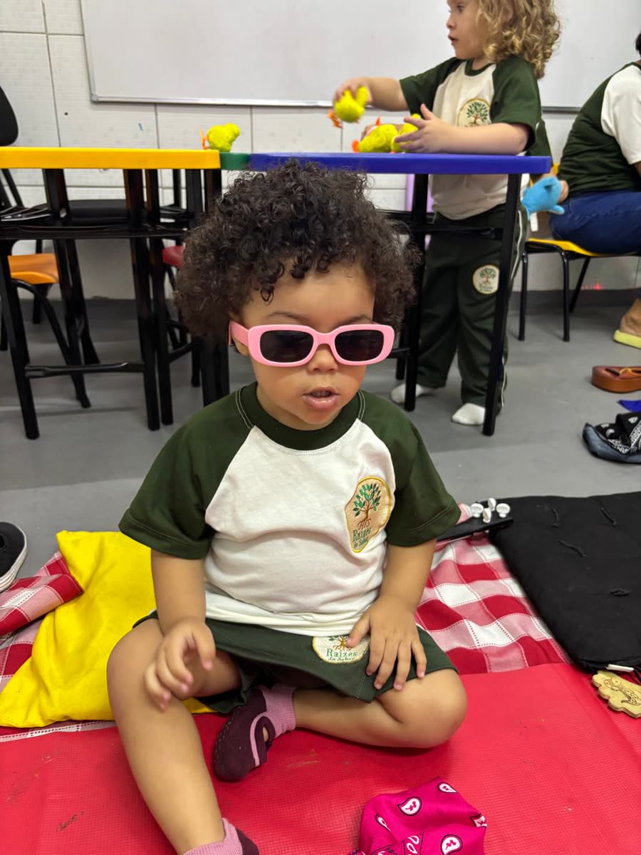 Criança da turma Berçário II com óculos de sol brincando na sala da Raízes do Saber
